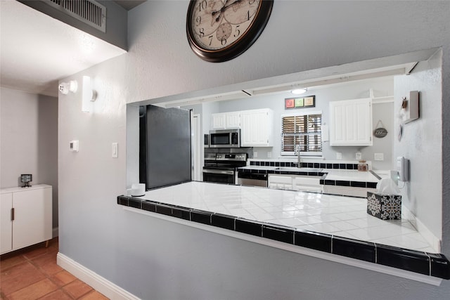 kitchen featuring sink, stainless steel appliances, tile counters, white cabinets, and light tile patterned flooring