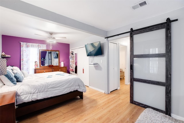 bedroom featuring light wood-type flooring, ceiling fan, a barn door, beam ceiling, and a closet