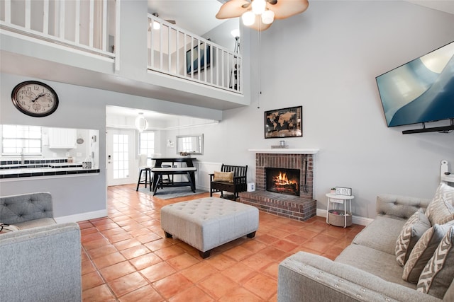 tiled living room with ceiling fan, a brick fireplace, and a high ceiling