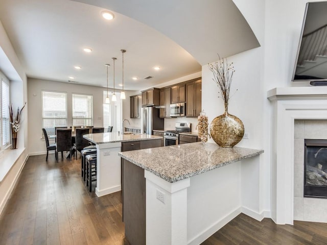 kitchen featuring stainless steel appliances, a kitchen island, dark hardwood / wood-style flooring, decorative light fixtures, and kitchen peninsula