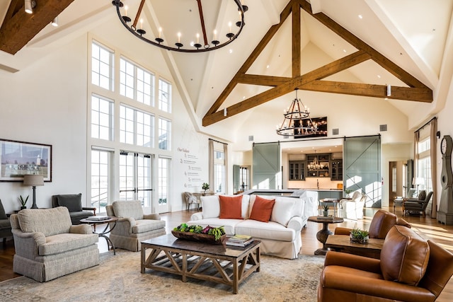 living room featuring hardwood / wood-style floors, beam ceiling, high vaulted ceiling, a notable chandelier, and a barn door