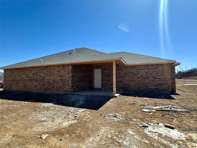 back of house with a shingled roof, brick siding, and a patio