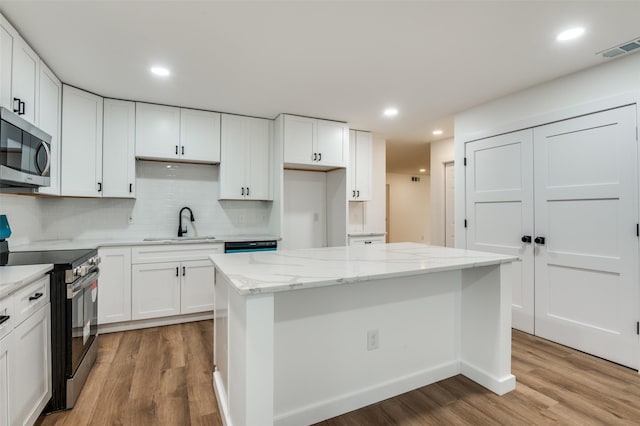 kitchen featuring sink, white cabinetry, a center island, stainless steel appliances, and backsplash