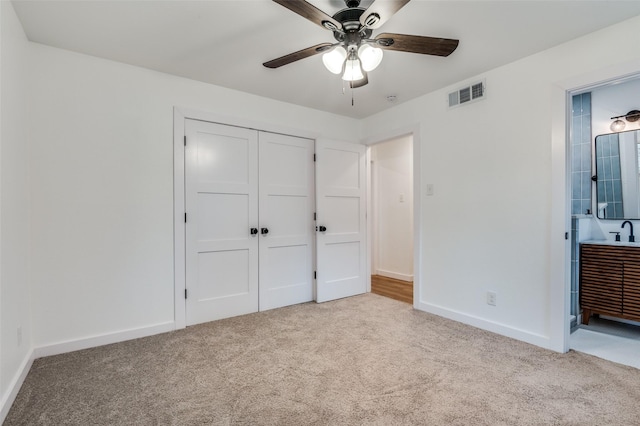 unfurnished bedroom featuring connected bathroom, sink, light colored carpet, ceiling fan, and a closet