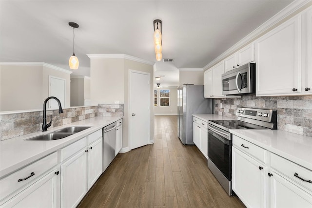 kitchen with sink, decorative light fixtures, ornamental molding, stainless steel appliances, and white cabinets