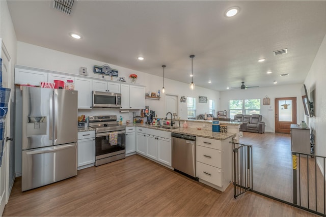 kitchen featuring appliances with stainless steel finishes, white cabinetry, decorative light fixtures, kitchen peninsula, and light wood-type flooring