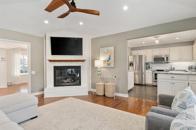 living room with dark hardwood / wood-style floors, ceiling fan, a fireplace, and vaulted ceiling