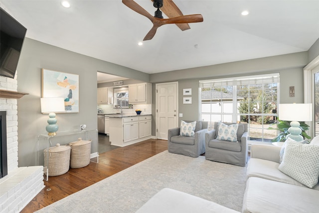 living room featuring dark hardwood / wood-style floors, a fireplace, lofted ceiling, sink, and ceiling fan