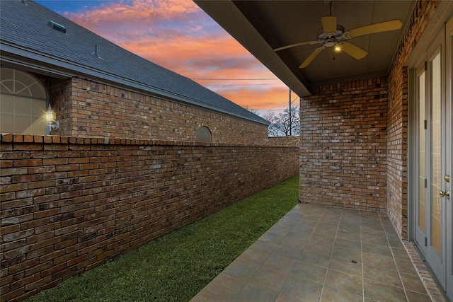 view of property exterior with ceiling fan, brick siding, a patio area, and a shingled roof