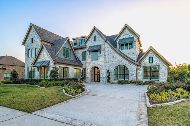 view of front facade featuring driveway, metal roof, a standing seam roof, a front yard, and brick siding