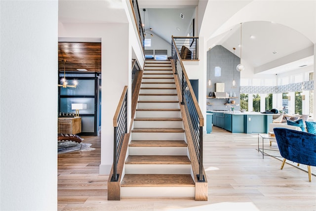 staircase featuring arched walkways, high vaulted ceiling, and wood finished floors