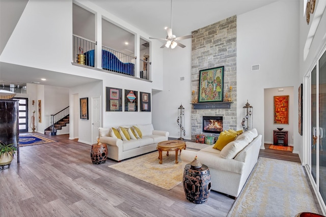 living room with hardwood / wood-style flooring, a towering ceiling, a stone fireplace, and ceiling fan