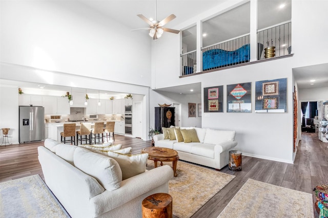 living room featuring ceiling fan, a towering ceiling, and wood-type flooring