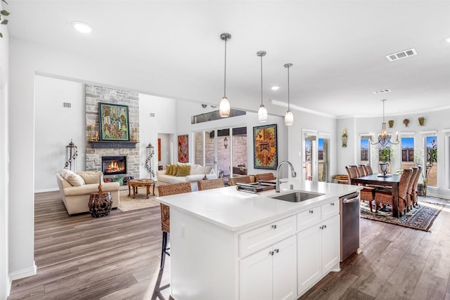 kitchen with sink, white cabinetry, hanging light fixtures, dishwasher, and an island with sink