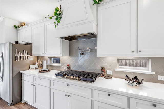 kitchen featuring appliances with stainless steel finishes, white cabinets, backsplash, custom range hood, and light wood-type flooring