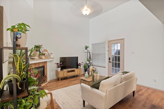 living room with a tiled fireplace, wood finished floors, and a towering ceiling