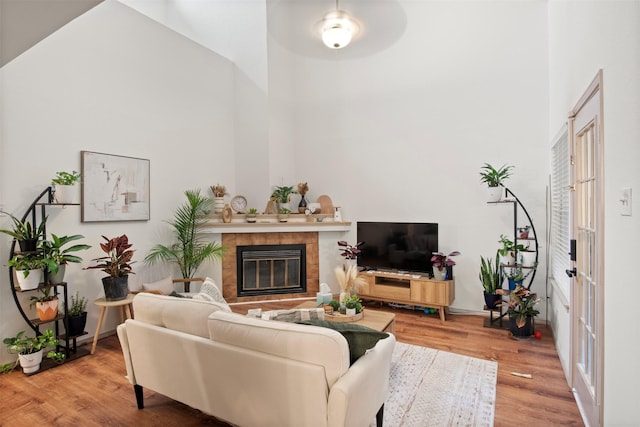 living room with a tiled fireplace, wood finished floors, and a towering ceiling