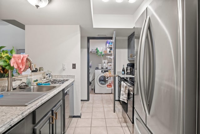 kitchen featuring gray cabinets, appliances with stainless steel finishes, separate washer and dryer, light tile patterned floors, and light stone counters