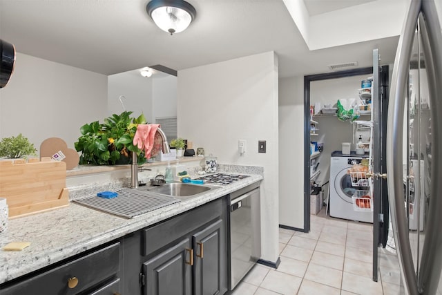 kitchen with light tile patterned floors, visible vents, appliances with stainless steel finishes, light stone countertops, and washer / dryer