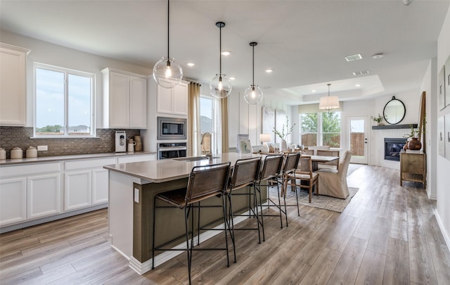 kitchen with decorative light fixtures, an island with sink, sink, white cabinets, and a tray ceiling