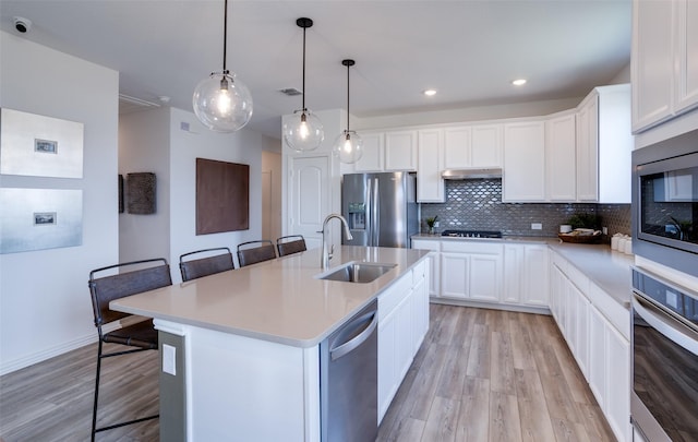 kitchen with a kitchen island with sink, sink, stainless steel appliances, and a kitchen bar