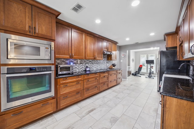 kitchen with tasteful backsplash, appliances with stainless steel finishes, sink, and dark stone counters