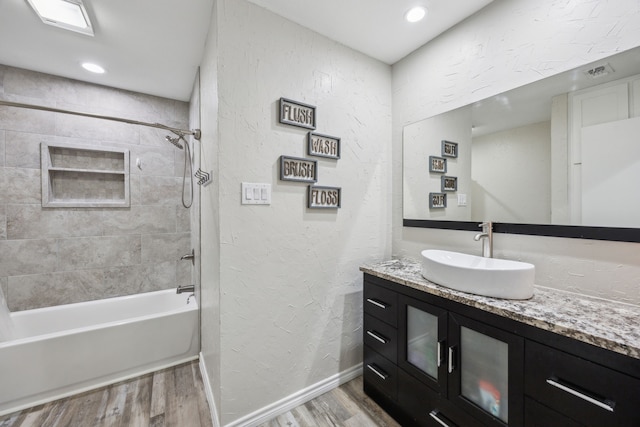 bathroom with hardwood / wood-style flooring, vanity, and tiled shower / bath