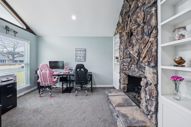 carpeted office space featuring lofted ceiling, a stone fireplace, and built in shelves