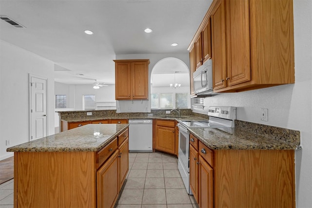 kitchen with dark stone countertops, a kitchen island, light tile patterned floors, and white appliances