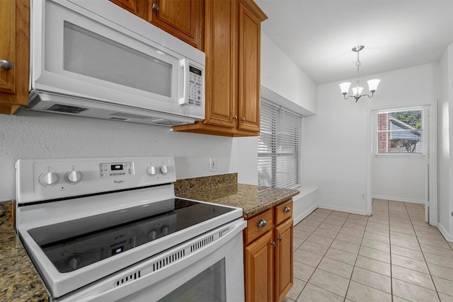 kitchen featuring light tile patterned flooring, pendant lighting, dark stone countertops, white appliances, and an inviting chandelier