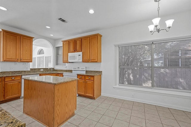 kitchen featuring white appliances, hanging light fixtures, a kitchen island, light stone counters, and light tile patterned flooring