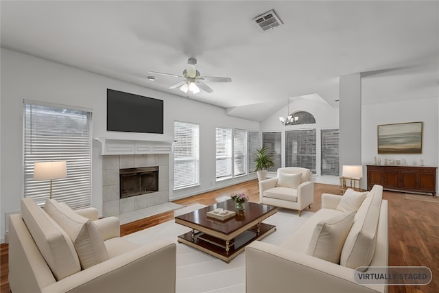 living room featuring lofted ceiling, hardwood / wood-style flooring, ceiling fan with notable chandelier, and a tile fireplace