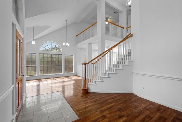 foyer entrance featuring hardwood / wood-style floors, ceiling fan with notable chandelier, and high vaulted ceiling