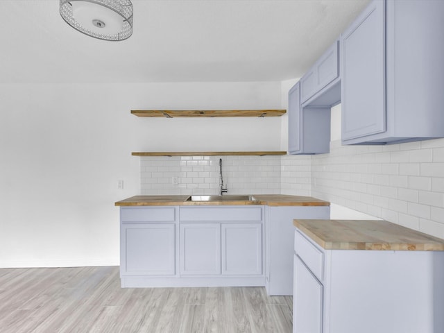 kitchen featuring tasteful backsplash, wood counters, sink, and light hardwood / wood-style flooring