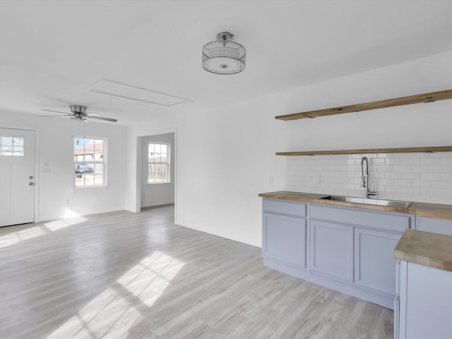 interior space featuring sink, decorative backsplash, ceiling fan, and light wood-type flooring