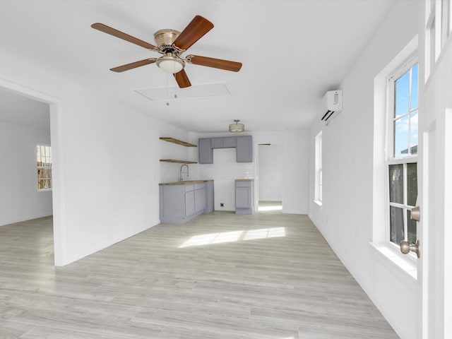 unfurnished living room with sink, a wall unit AC, and light hardwood / wood-style flooring