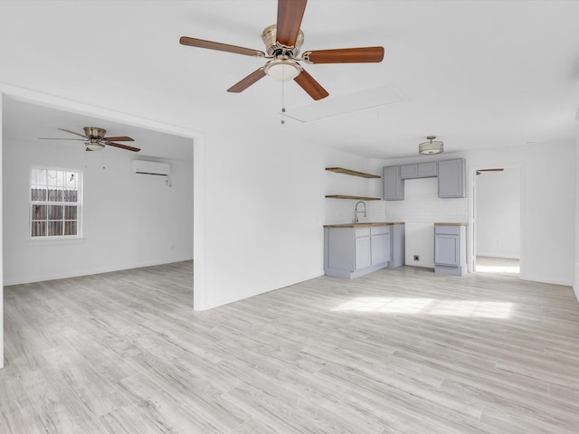 unfurnished living room featuring light wood-type flooring, ceiling fan, sink, and an AC wall unit