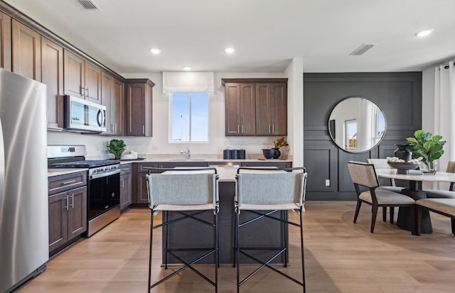 kitchen with stainless steel appliances, a center island, dark brown cabinets, and light wood-type flooring