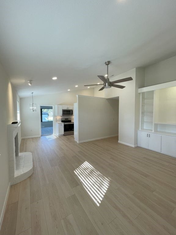 unfurnished living room featuring ceiling fan with notable chandelier, a fireplace, and light hardwood / wood-style floors