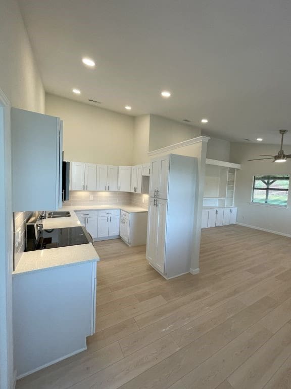 kitchen featuring light wood-type flooring, white cabinets, ceiling fan, decorative backsplash, and a high ceiling