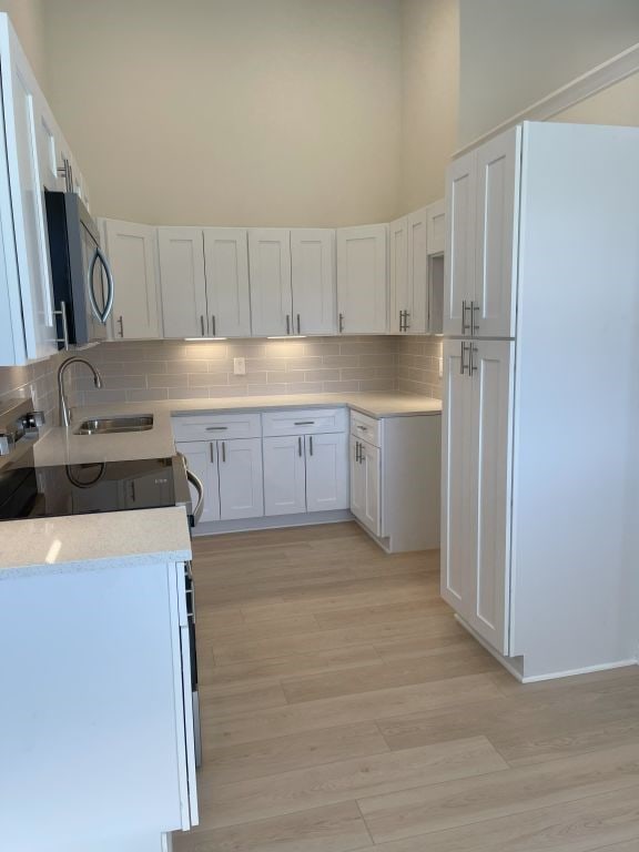 kitchen featuring sink, light wood-type flooring, range with electric stovetop, decorative backsplash, and white cabinets