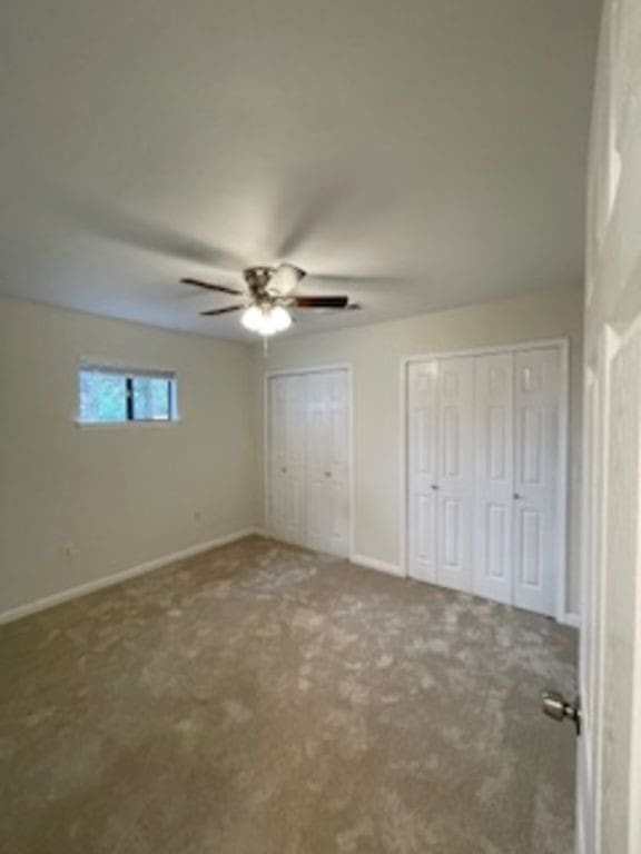 unfurnished bedroom with ceiling fan, carpet flooring, and two closets