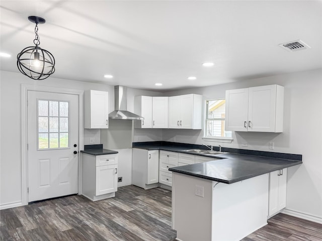 kitchen featuring wall chimney range hood, pendant lighting, white cabinets, and kitchen peninsula