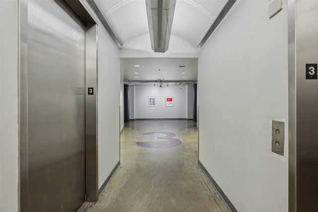 corridor featuring elevator, lofted ceiling, and brick ceiling