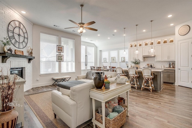 living room featuring a brick fireplace, light hardwood / wood-style floors, and ceiling fan