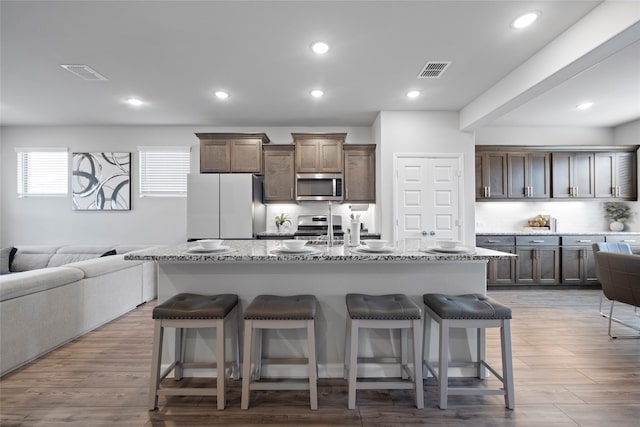 kitchen featuring a breakfast bar, wood-type flooring, stainless steel appliances, a kitchen island with sink, and backsplash