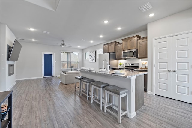 kitchen featuring a kitchen bar, light stone counters, a center island with sink, light hardwood / wood-style flooring, and stainless steel appliances