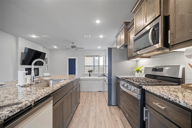 kitchen with sink, appliances with stainless steel finishes, backsplash, light stone counters, and light wood-type flooring