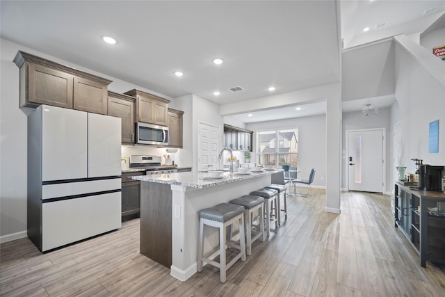 kitchen with a breakfast bar, light stone counters, a kitchen island with sink, stainless steel appliances, and light hardwood / wood-style floors