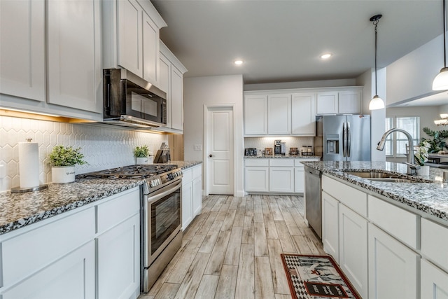 kitchen featuring sink, light hardwood / wood-style flooring, hanging light fixtures, stainless steel appliances, and white cabinets